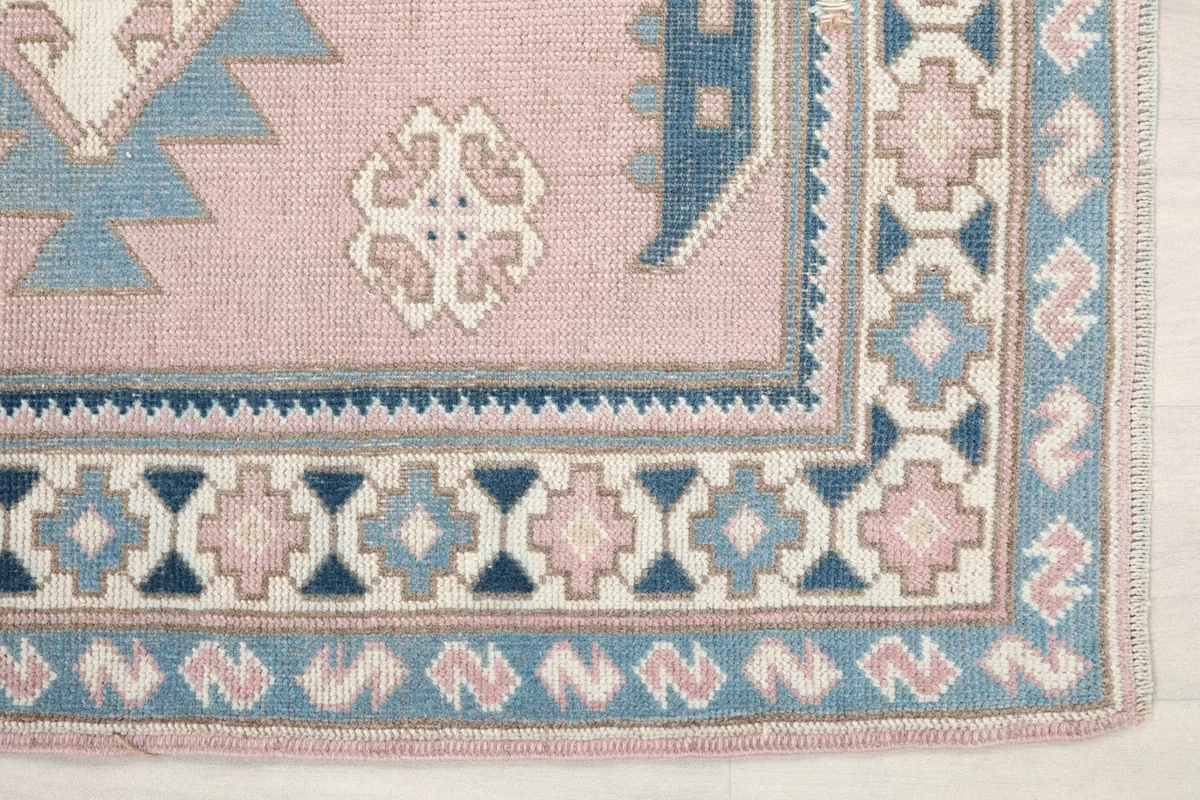 Detailed view of the corner of the rug, highlighting the intricate blue and pink border designs