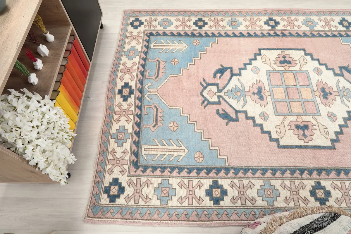 Side angle view of the rug, revealing the soft pink field and contrasting blue and ivory border