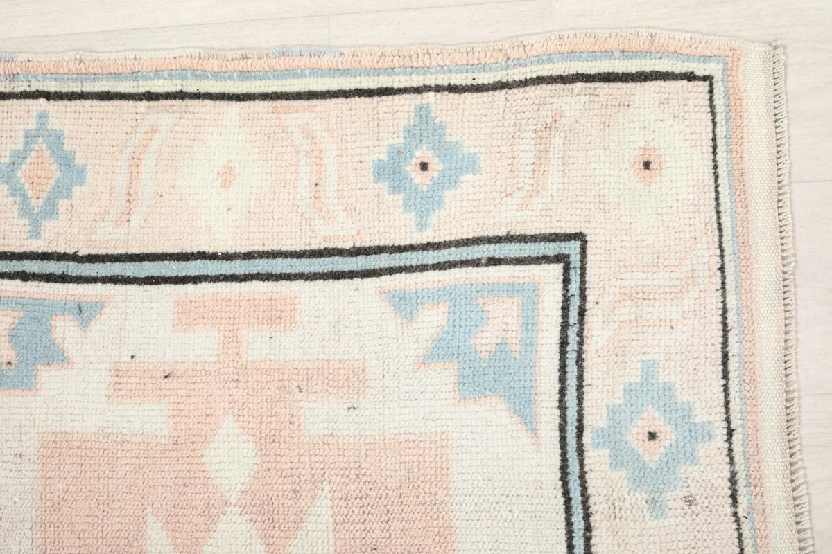 Corner detail of the rug, highlighting the ivory, rose, blue, and black border.