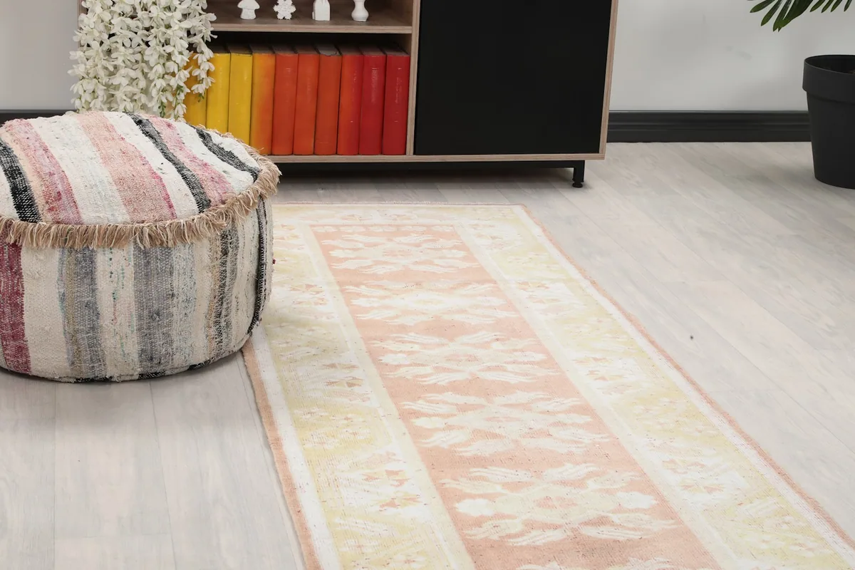 Close-up view of the runner rug's pink field and cream geometric motifs next to a pouf