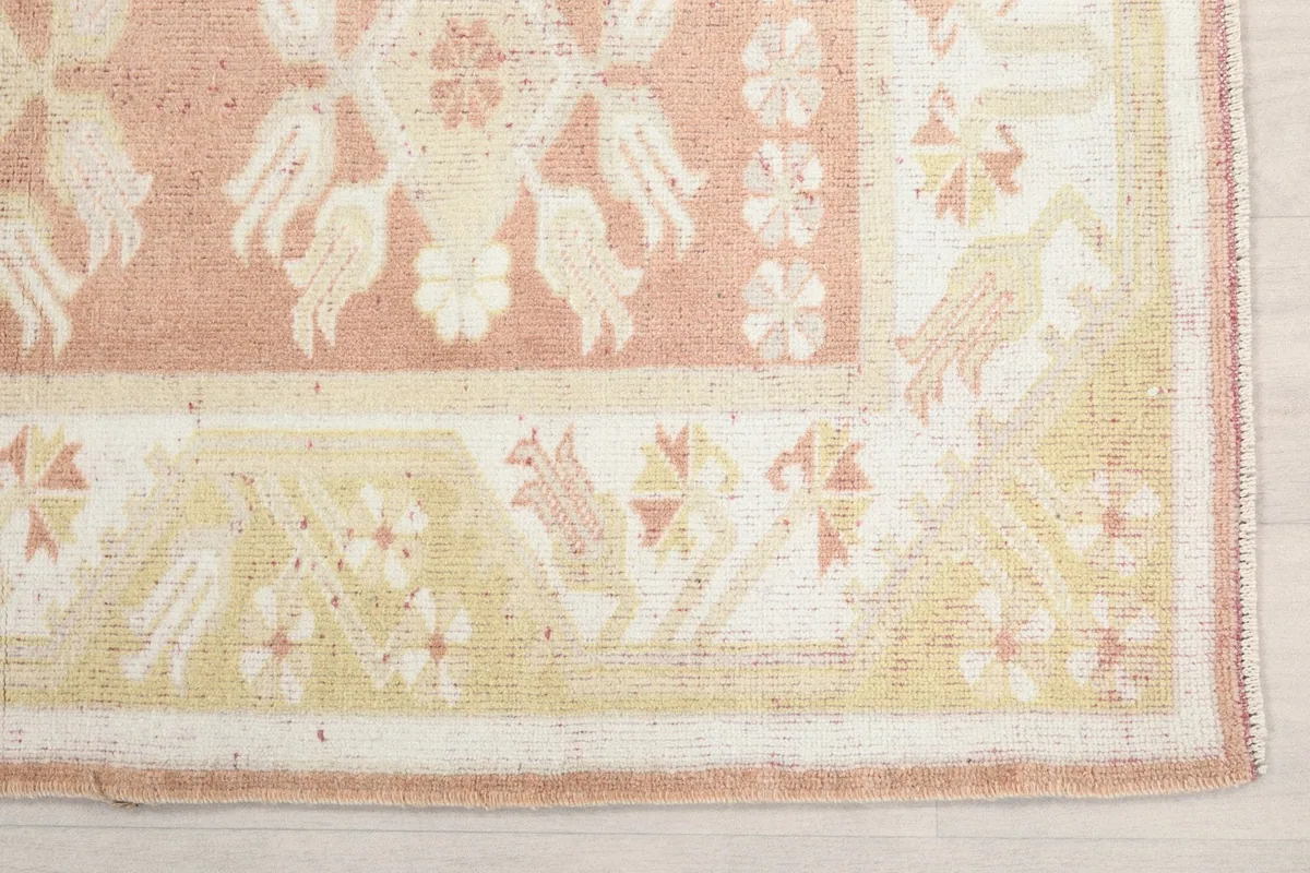 Detailed shot of the corner of the rug, showing the yellow border and pink field with motifs