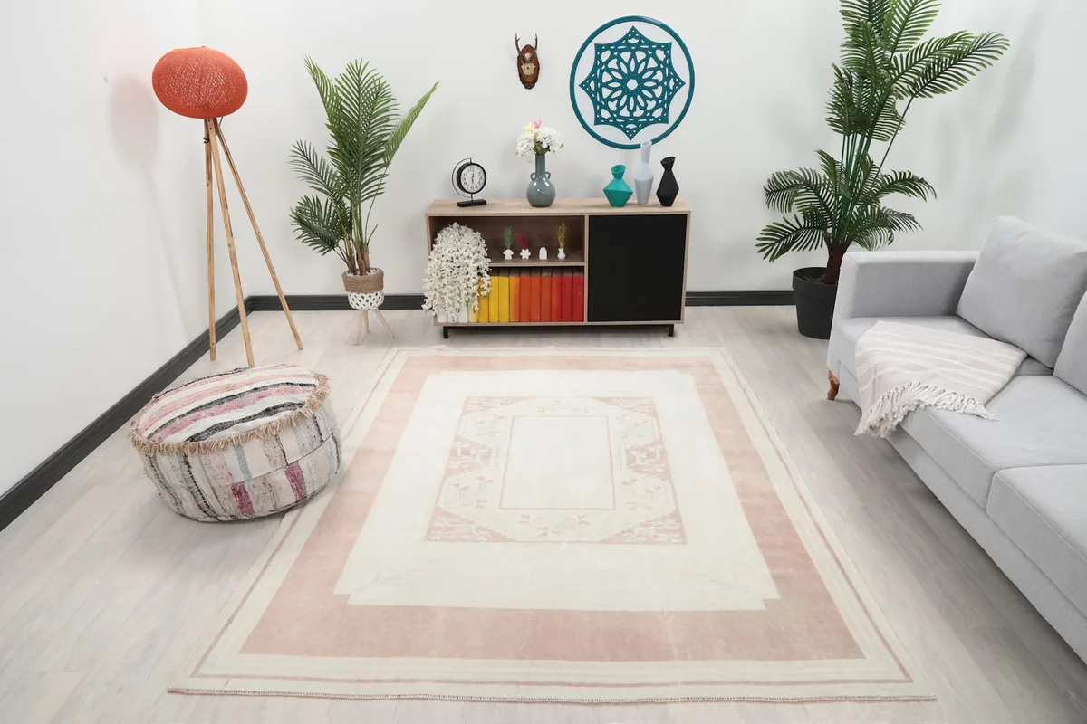 Ivory and pink rug placed in a living room setting with a light gray sofa and wooden furniture