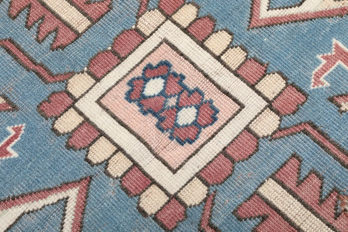 Extreme close-up showing the hand-knotted wool pile texture and the faded blue and rose colors.