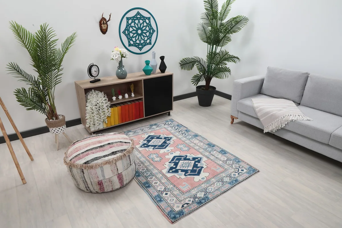 Vintage Anatolian rug with pink and blue patterns shown in a bright room with plants and furniture.