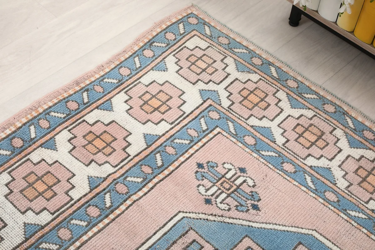Angled view showing the rug's border design, including rose, blue, and ivory geometric shapes