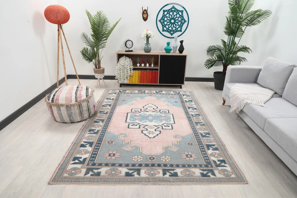Vintage pink and blue rug displayed in a bright living room setting with a sofa and plants