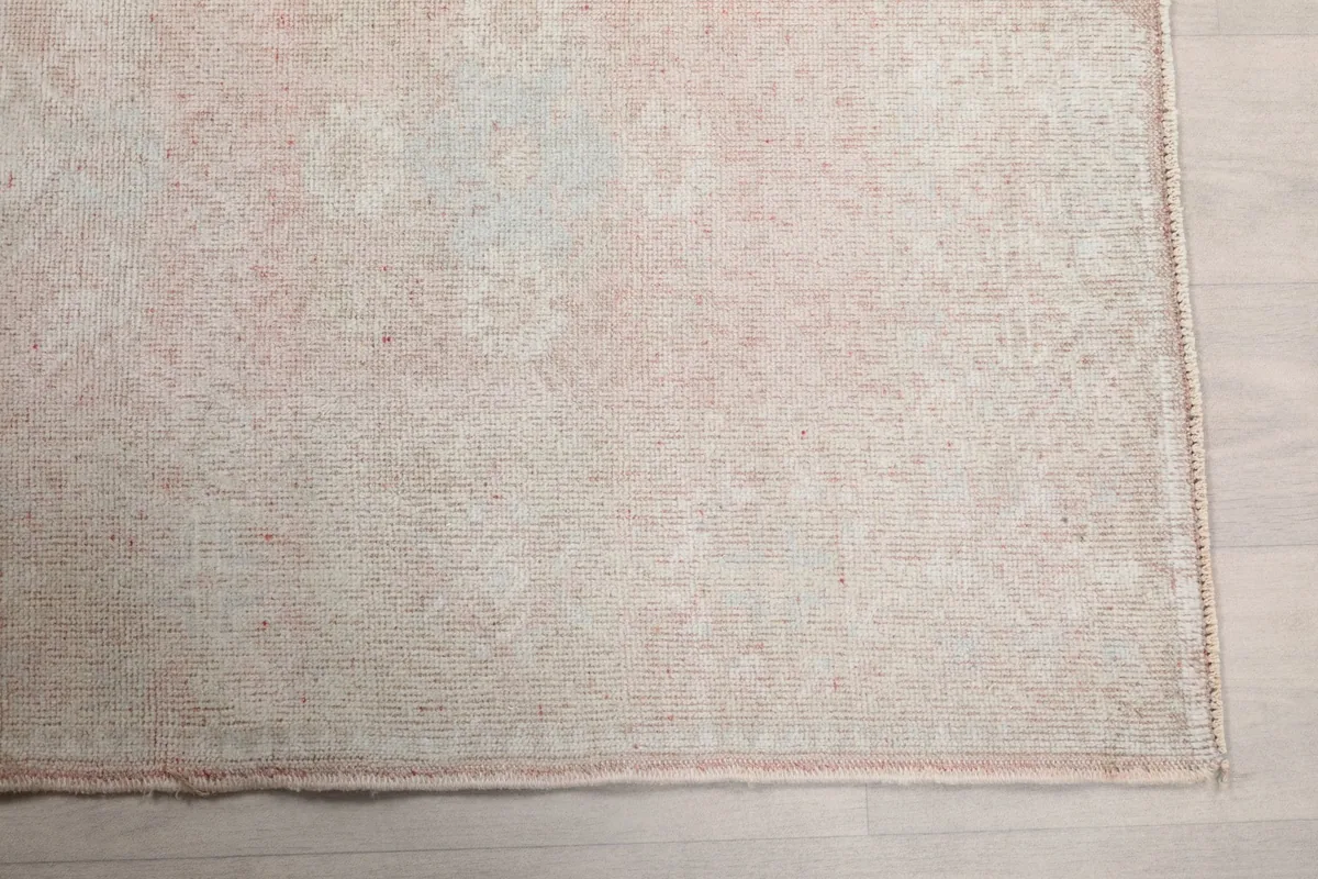 Detailed view of the rug's corner, showing the subtle rose tones and low pile texture