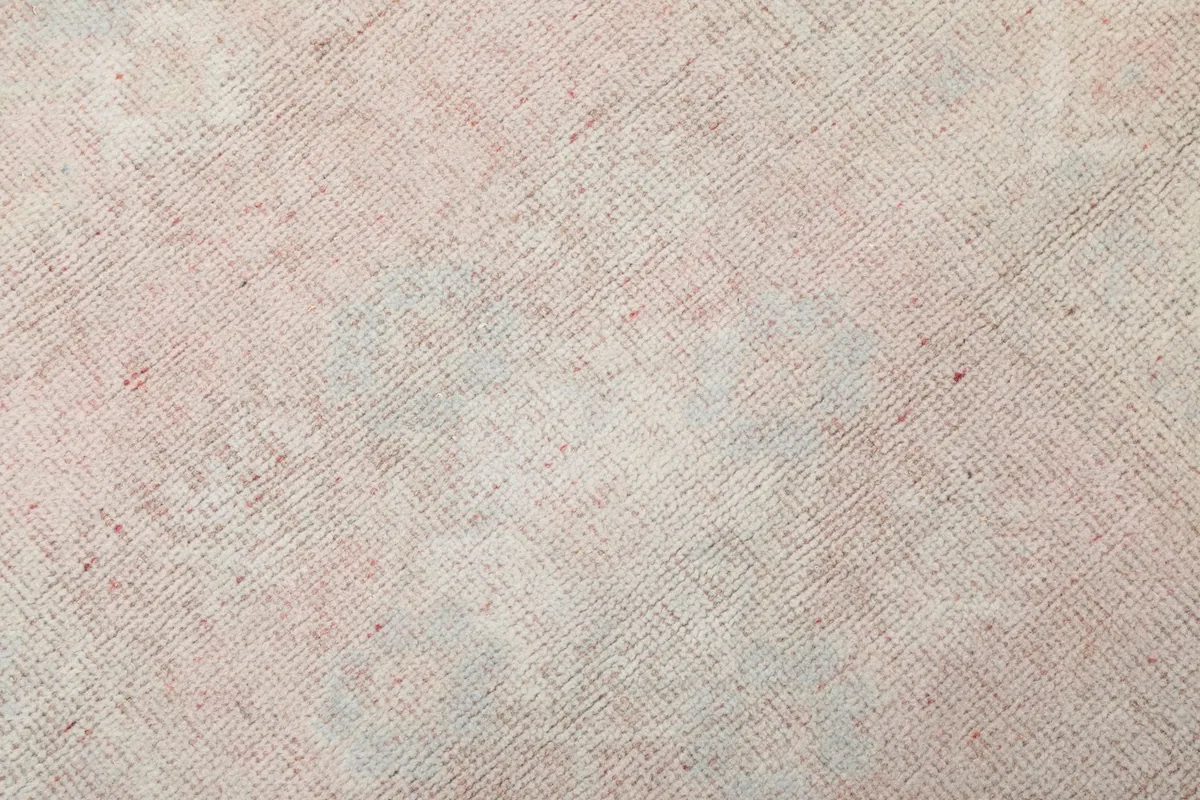 Close-up of the rug's low wool pile, revealing faded geometric motifs in beige, rose, and blue