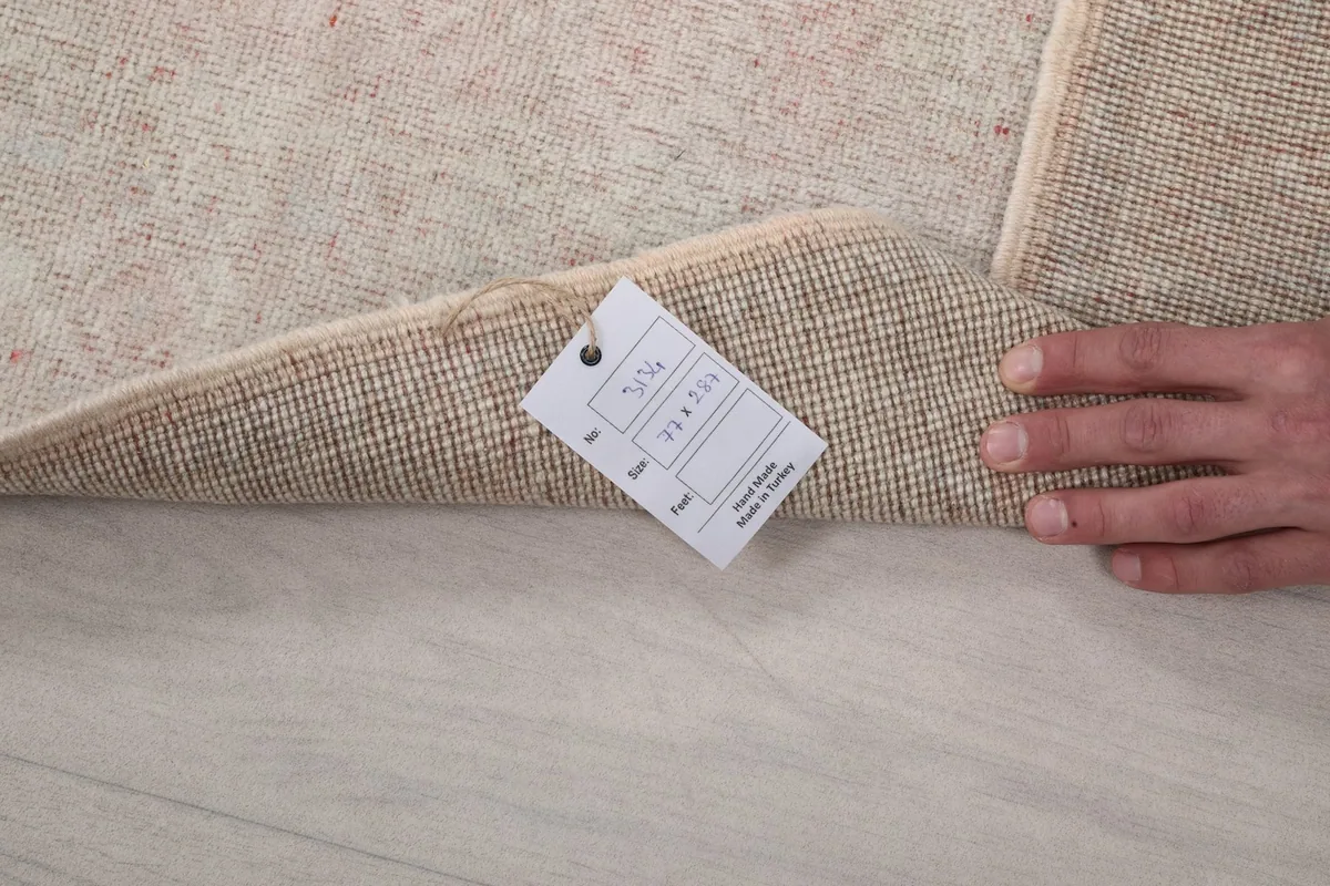 Hand holding the rug to show the back and a product tag indicating origin and size