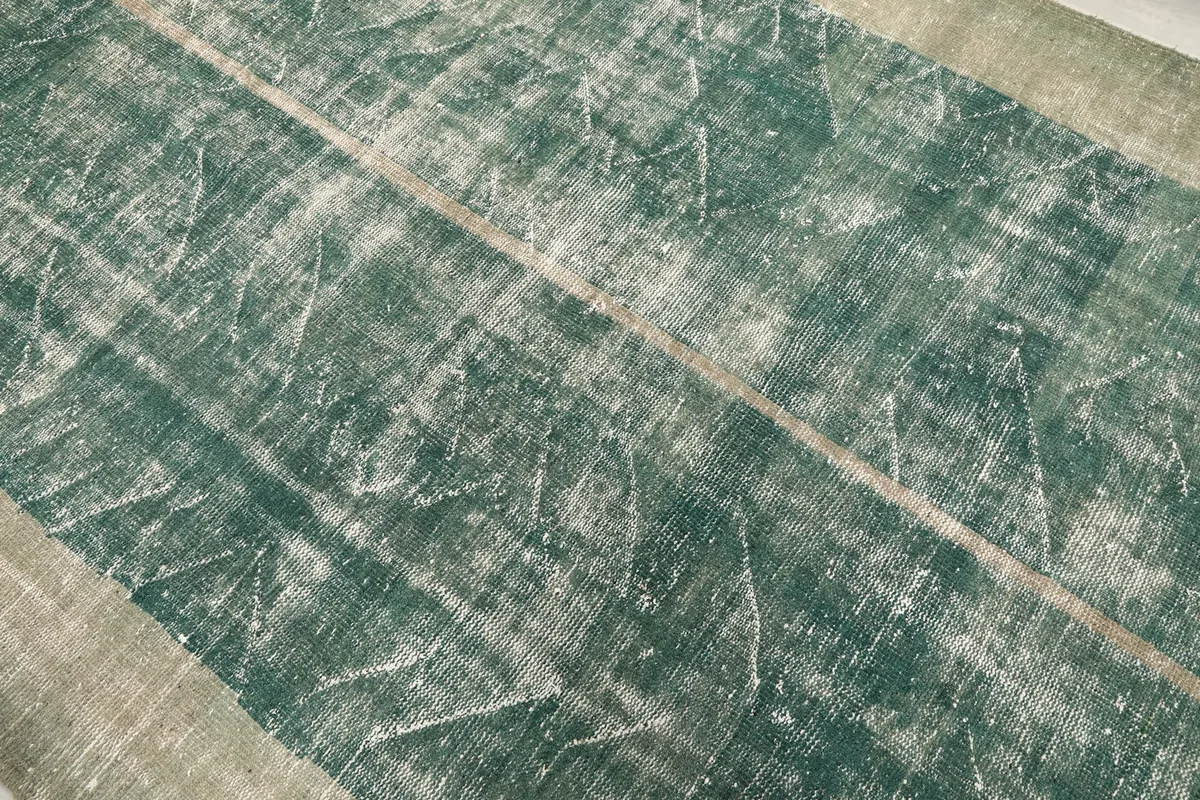 Close-up of the distressed green pile with subtle geometric patterns and central seam