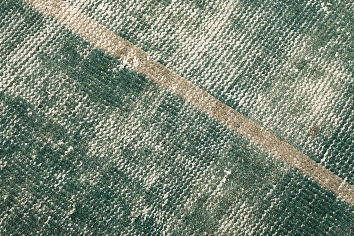 Detailed view of the low wool pile texture and distressed finish of the green rug