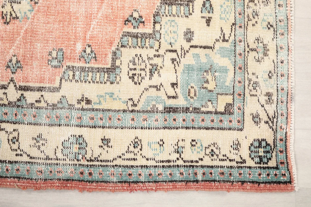 Detail of the ivory border with blue geometric motifs and the rose field of the hand-knotted rug.