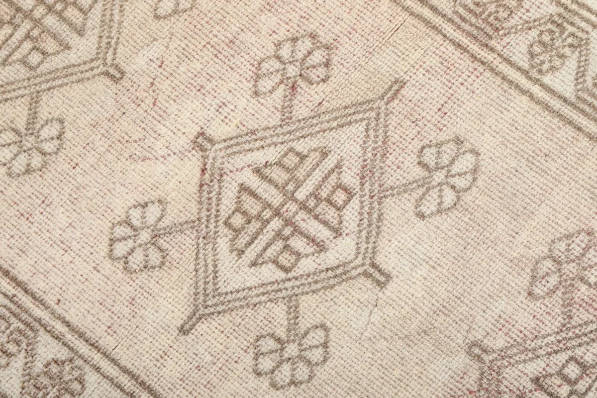 Close-up of a central tan geometric motif against the beige field, showing knot detail.