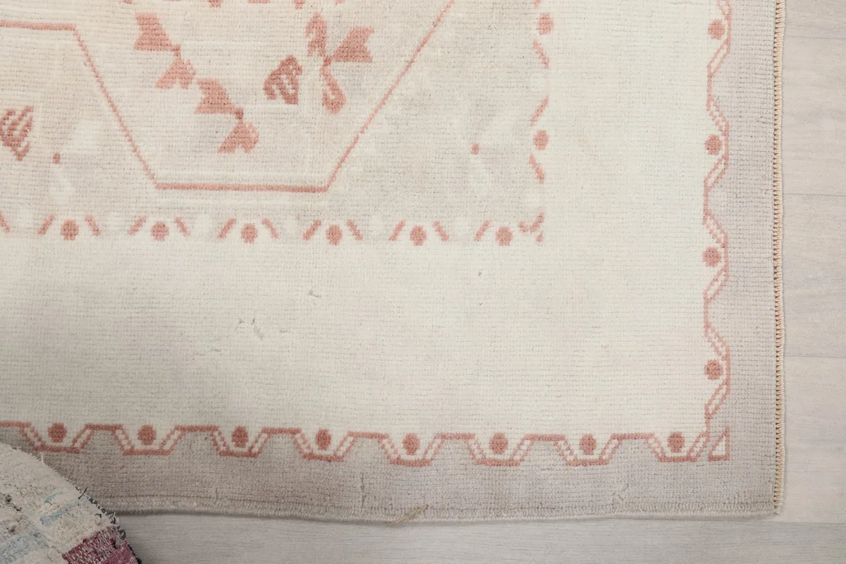 Detail view of the rug's border design and corner with geometric motifs in pink