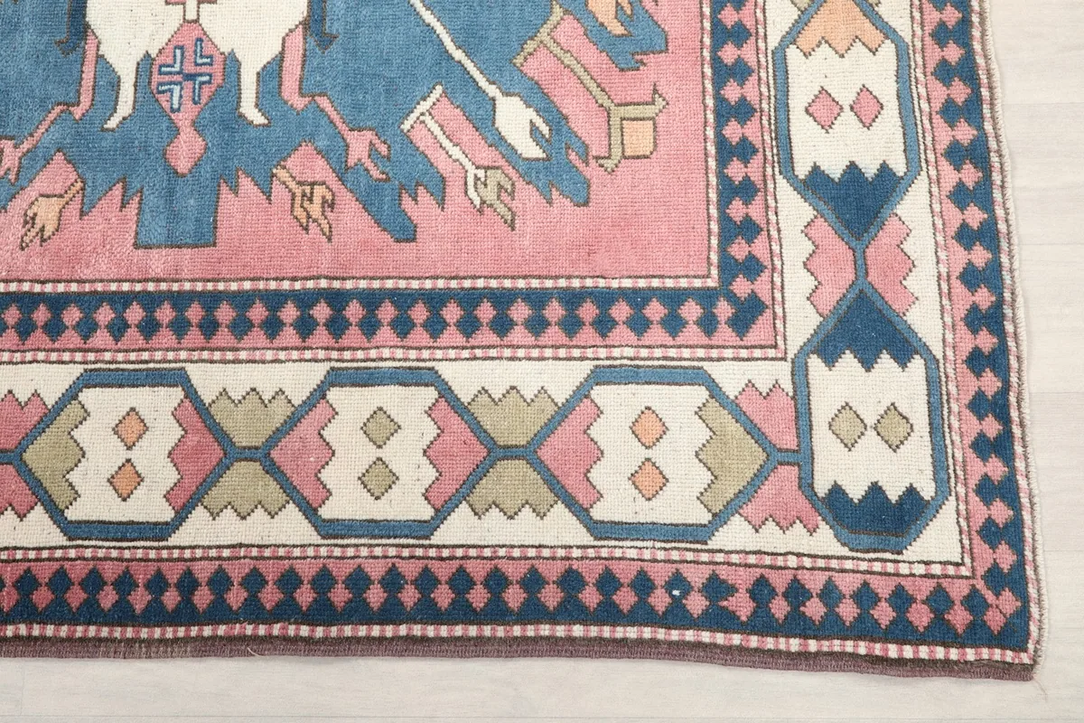 Detail of the rug's border design featuring geometric shapes in pink, blue, and ivory tones