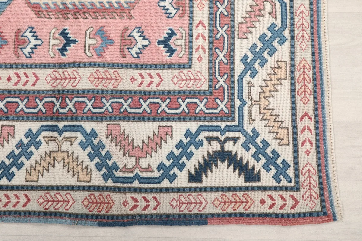 Close-up of a corner section of the rug, showing cream, blue, and rust geometric border details.