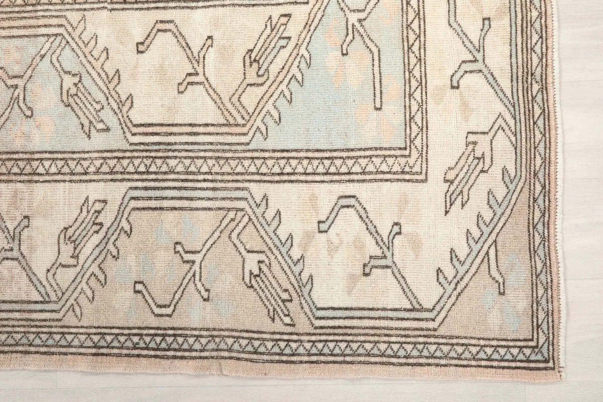 Detail of the rug's geometric border pattern in cream and charcoal with subtle blue accents