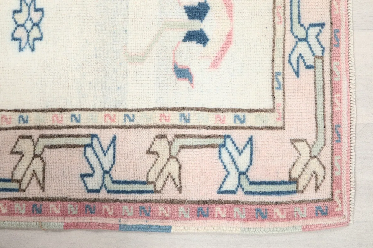 Detailed corner view of the pink border and blue geometric motifs on the rug