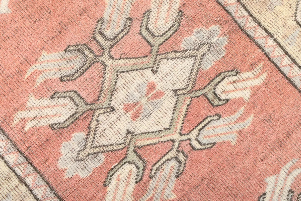 Close-up of a central geometric motif in shades of rose, ivory, and gray on the rug