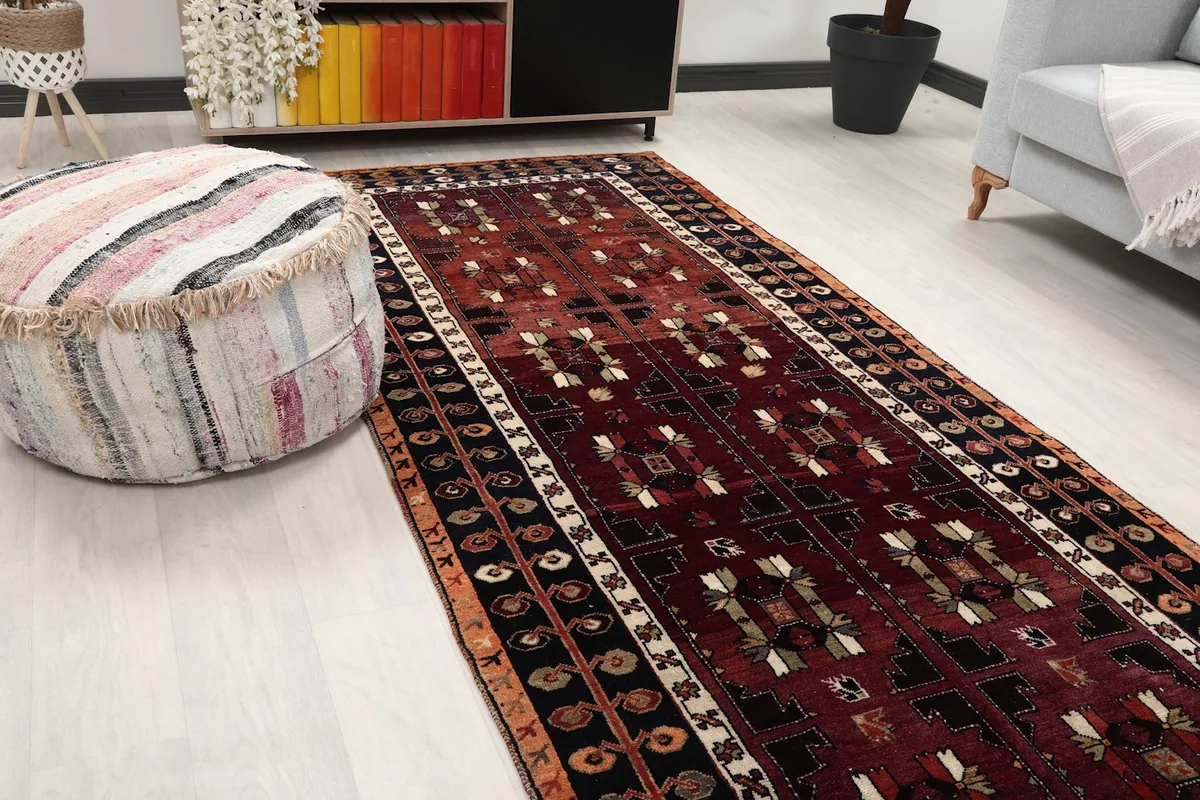 Close-up of the runner rug in a room, showing the red field and geometric patterns near a pouf