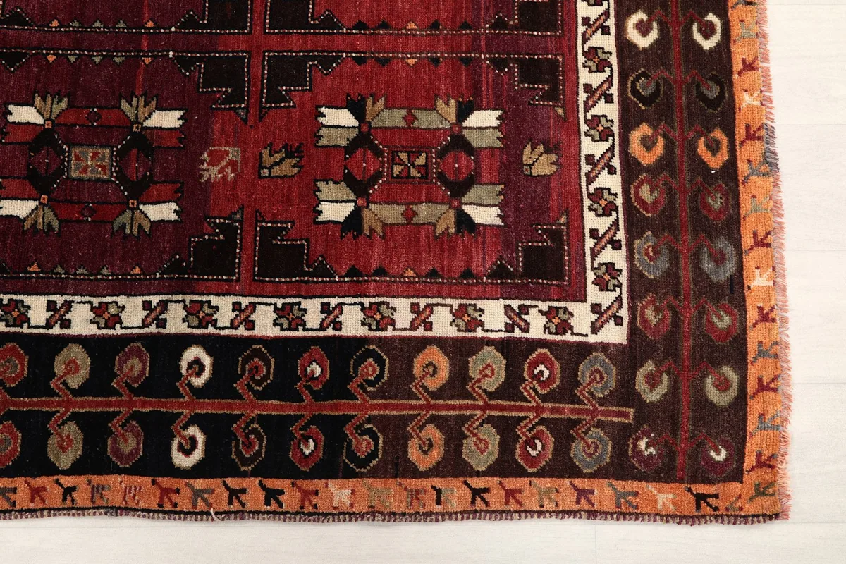 Detailed view of the rug's corner, showing red field, navy border, and intricate tribal motifs
