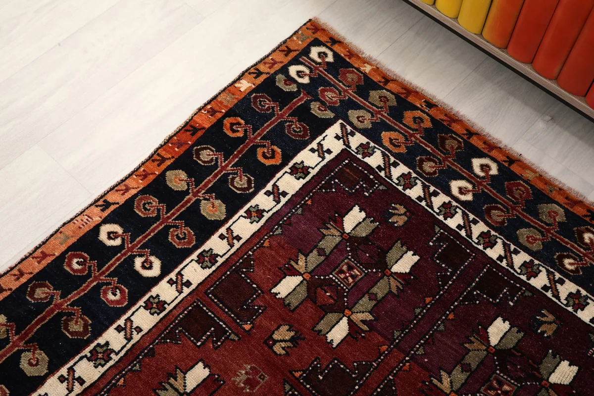 Detail of the rug's border, featuring navy, ivory, and tan patterns on the red background