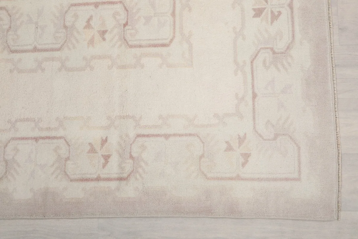 Detail of the rug's border showing faded cream and rose tones