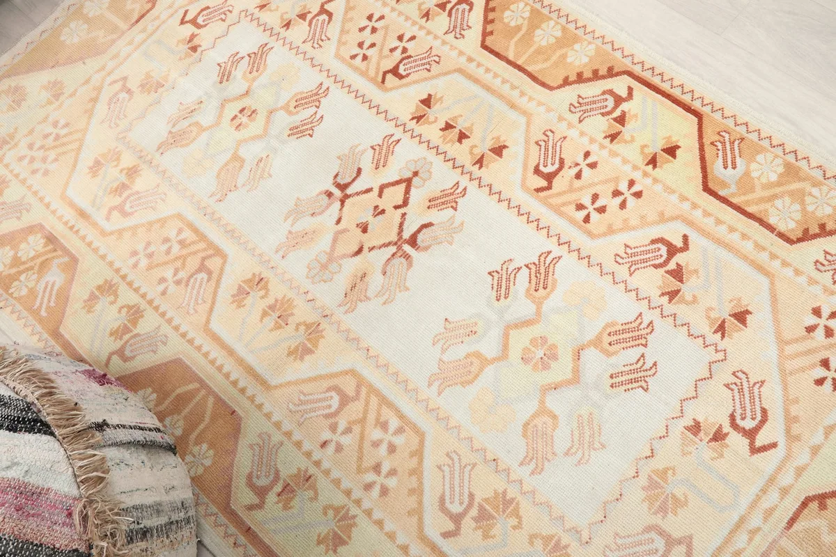 Overhead angle showing the central design and border of the ivory and orange vintage rug
