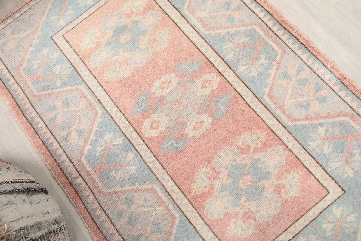 Diagonal view showing the rose central field and blue geometric border of the rug