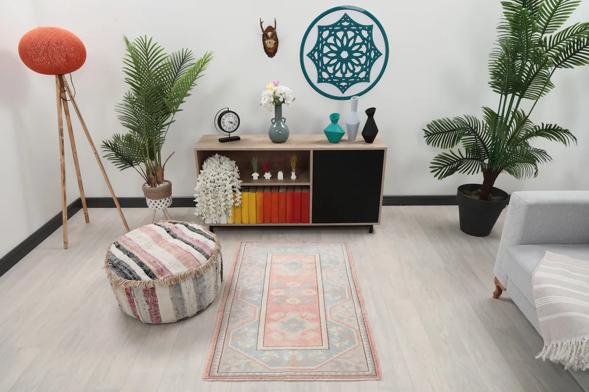 Rose and blue rug styled in a room setting with a pouf and plants