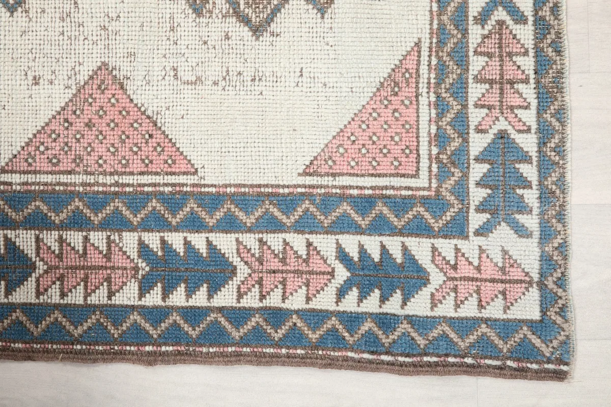 Detailed view of the rug's corner, showing pink triangles and blue tree motifs in the border
