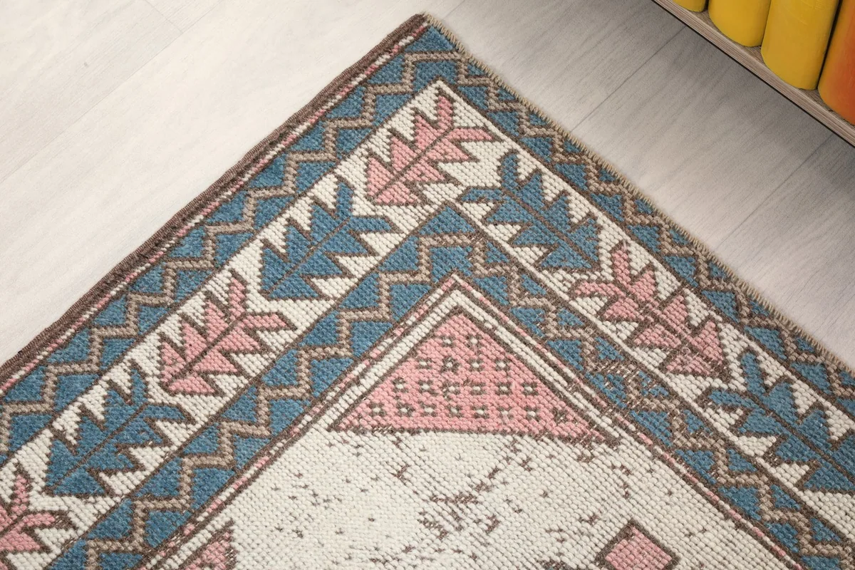 Close-up of a rug corner, detailing the layered geometric border patterns in pink and blue