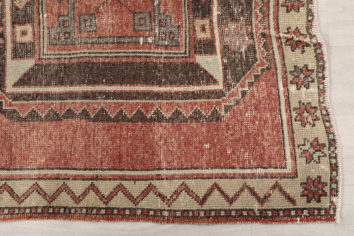 Close-up of the rust field and beige border with a zigzag pattern and floral motifs.