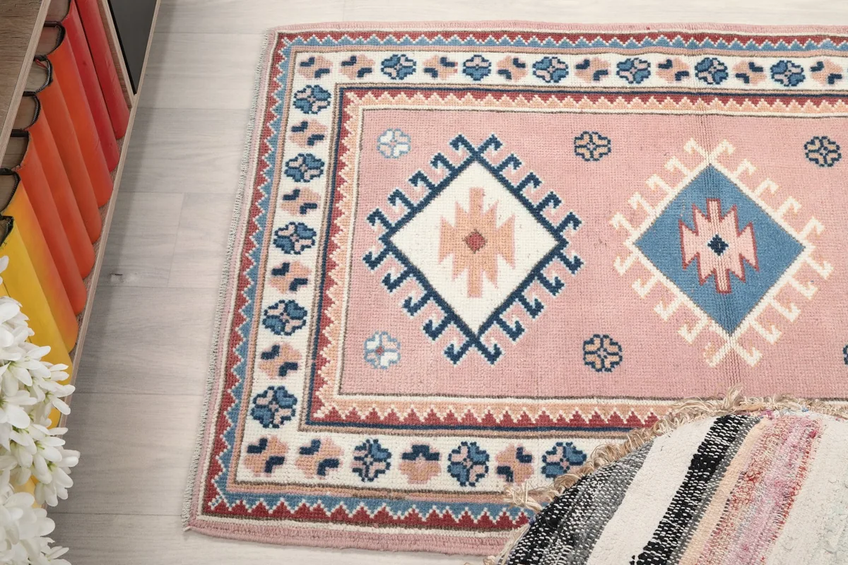 Angled view of the rug, capturing the interplay of the pink field and border details