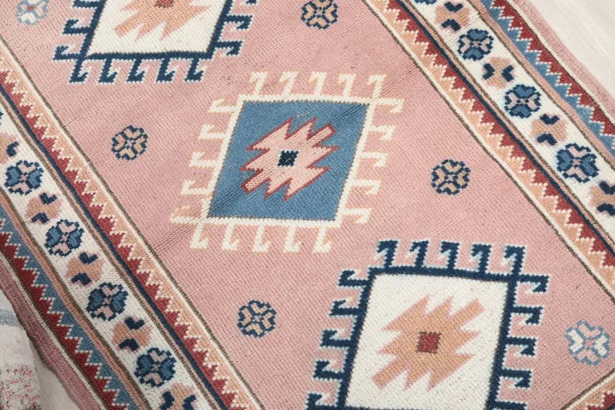Close-up of the central geometric diamond motifs in blue, ivory, and rust on the pink field