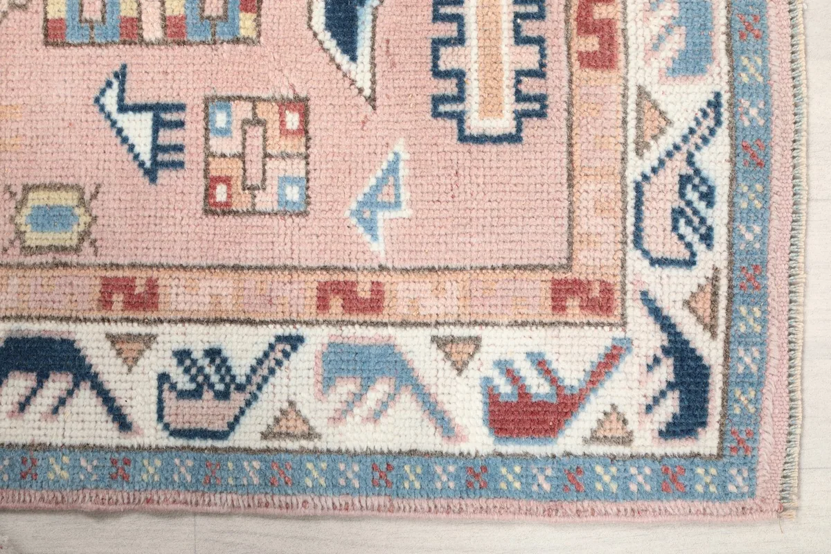 Detailed view of the corner of the rose rug, showing geometric and bird motifs in blue and red.