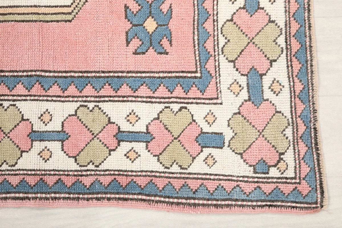Detail of the rug's border with repeated geometric flower-like motifs in pink, tan, and blue