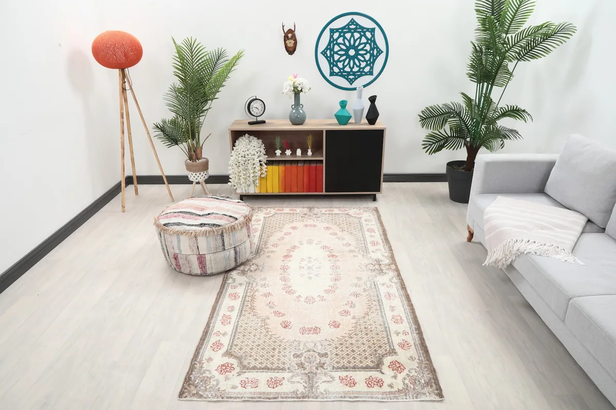 Ivory and rose vintage rug styled in a modern living room setting with a sofa and pouf