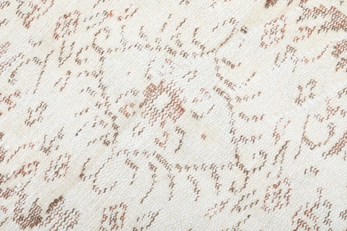 Close-up of the low wool pile, revealing the texture and the faded, tonal beige and tan patterns.