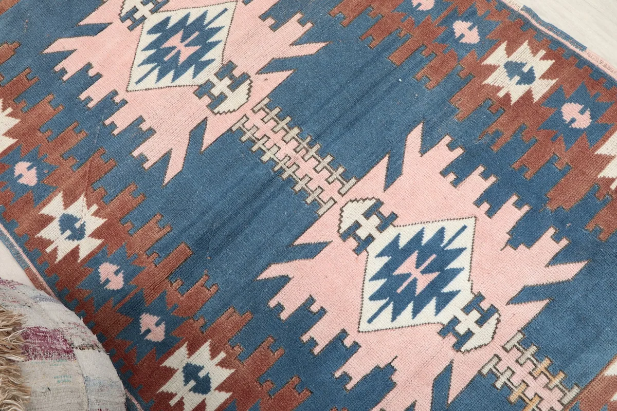 Angled view of the rug's surface, capturing the interplay of blue, rust, and pink geometric designs.