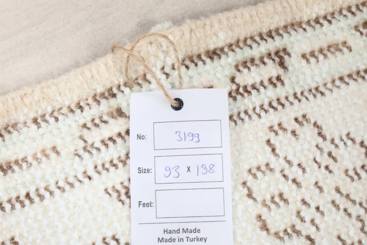 Close-up of the rug's tag, indicating its size as 93 x 198 cm and handmade origin