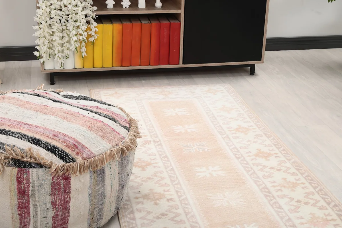 Close-up of the runner rug showing rose and beige geometric patterns next to a pouf