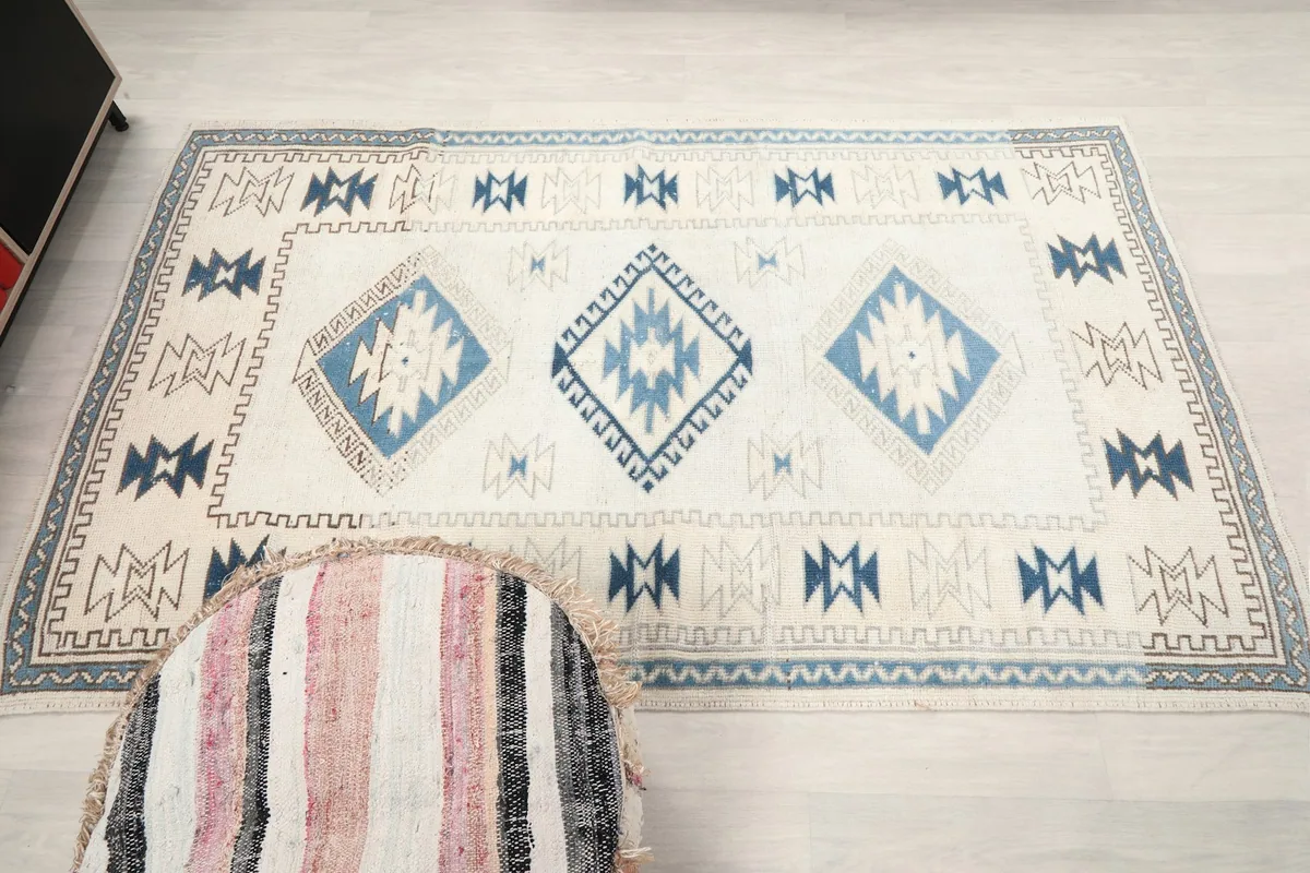 Full overhead view of the 4x7 ivory and blue vintage rug, illustrating its symmetrical tribal design.