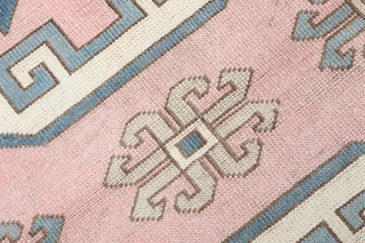 Close-up detail of a small, stylized geometric motif on the pink field of the rug.