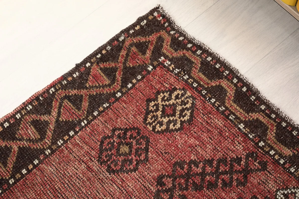 Corner detail of the rug, highlighting the charcoal border and rust field with subtle wear