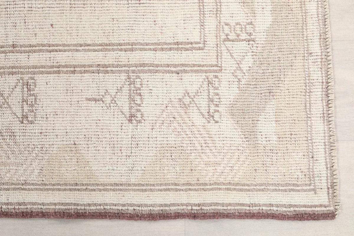 Detailed view of the rug's corner, highlighting the geometric patterns and the rose-colored border.
