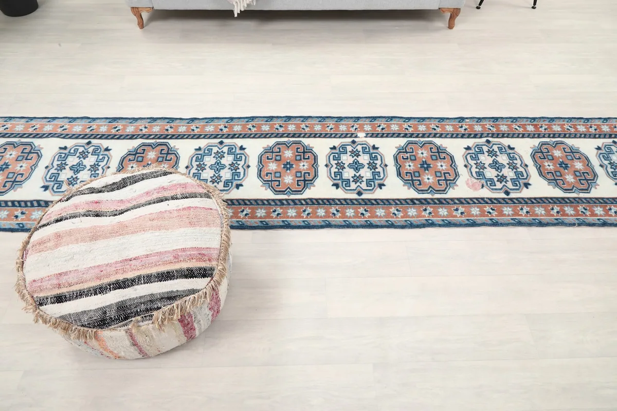 Long view of the vintage runner rug stretching across a light-colored floor, with a pouf in the foreground