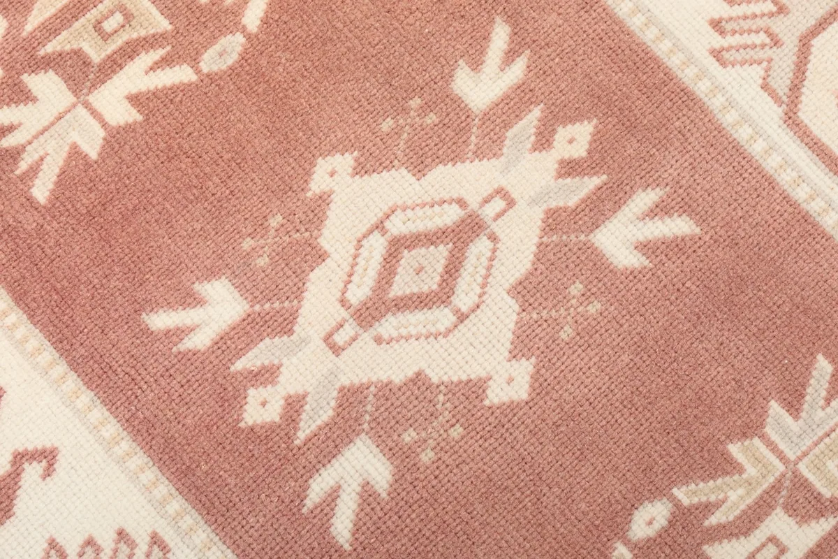 Macro detail of a single ivory geometric motif on the rose background of the runner