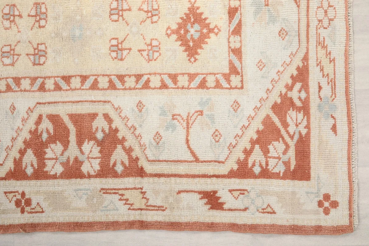 Detailed view of the rust border and ivory field patterns at the corner of the rug