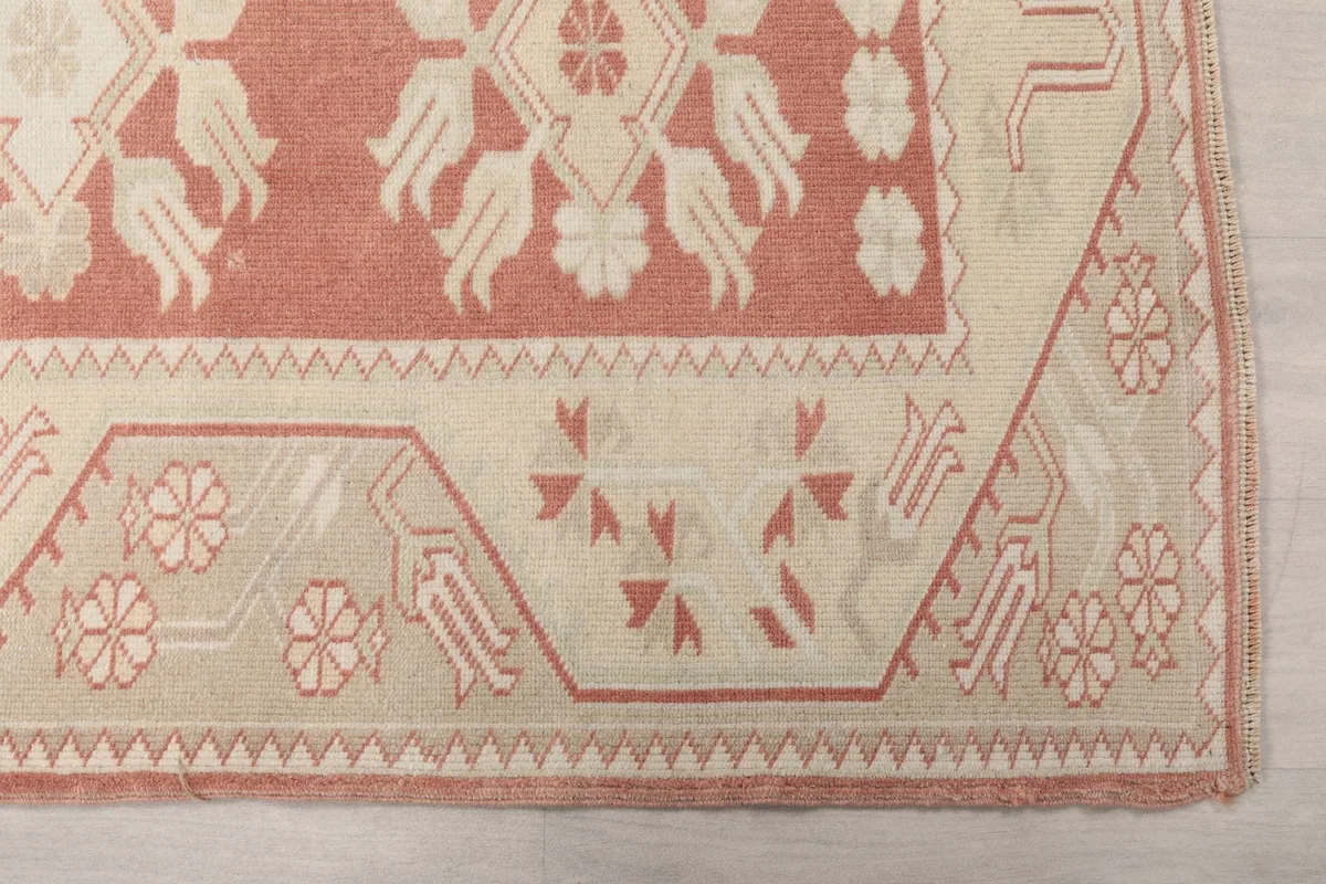 Close-up detail of the geometric border and corner motifs in ivory and rose tones.
